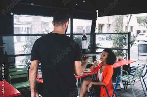 Male waiter bringing wine to table of female visitor