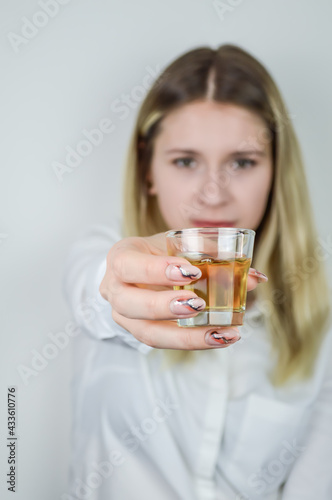 Portrait of a beautiful young blonde woman holding a shot of liqueur in front of her - Focus on the shot