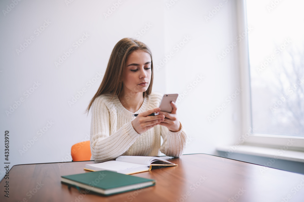 Wistful woman browsing smartphone while studying Wistful woman browsing smartphone while studying