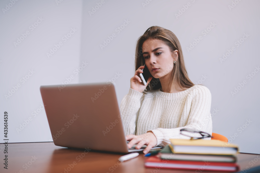 Serious young freelancer having phone call while working on laptop Serious young freelancer having phone call while working on laptop