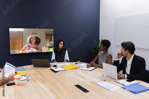 Diverse group of business colleagues having video call with businesswoman on screen in meeting room