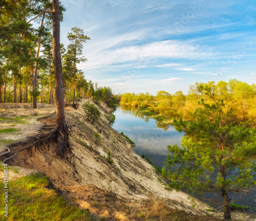 Panoramic photo of the river with steep banks and pine trees on the cliff. Rest in tents in nature.