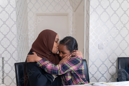 Black Muslim mother kissing daughter's forehead