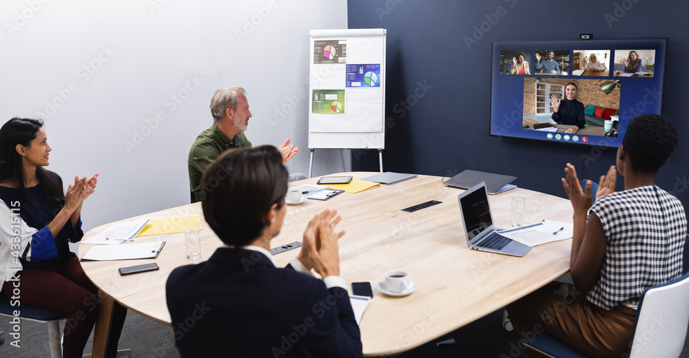 Diverse group of business colleagues having video call with coworkers on screen in meeting room