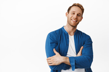 Cool handsome redhead man, smiling with confidence, cross arms on chest and looking happy unbothered, standing in casual relaxed pose against white background