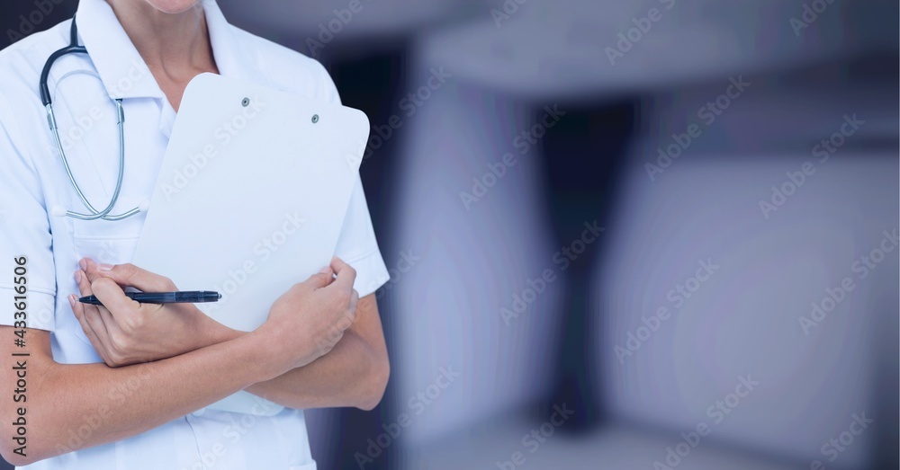 Composition of midsection of female doctor in lab coat holding clipboard over out of focus hospital