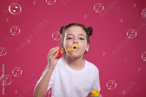 Little girl blowing soap bubbles on pink background