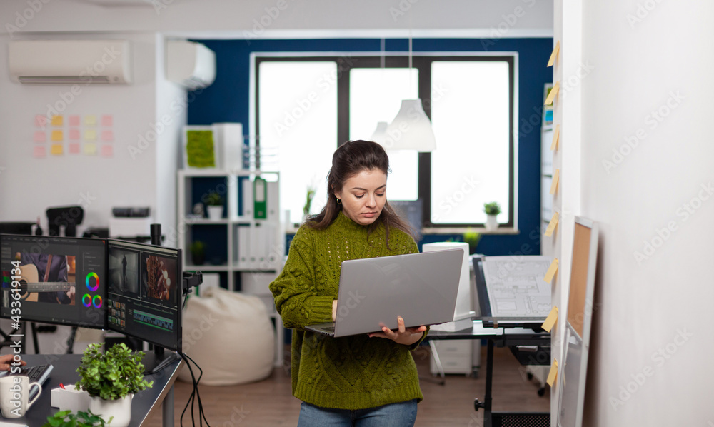 Employee holding laptop standing in creative agency office prosessing customer video project in post production software. Videographer working in digital multimedia company editing movie footage Employee holding laptop standing in creative agency office prosessing customer video project in post production software. Videographer working in digital multimedia company editing movie footage