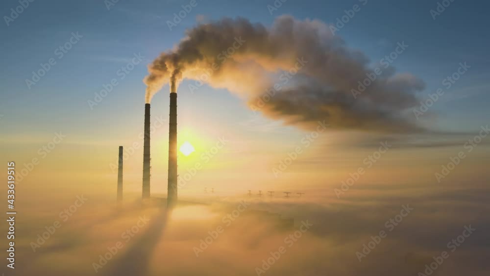 Aerial view of coal power plant high pipes with black smoke moving up polluting atmosphere at sunset.