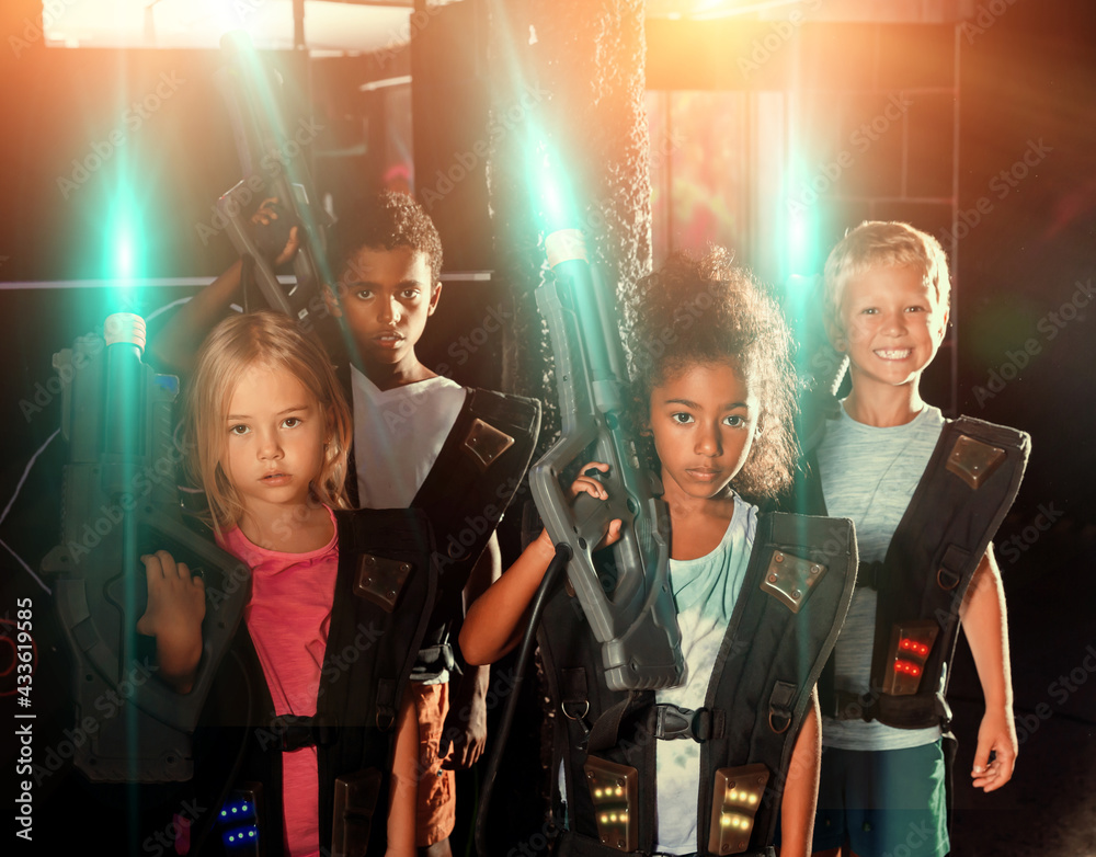 Portrait of multiracial group of happy preteen kids with laser guns during lasertag game in dark room