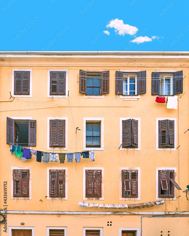 Picturesque typical Italian slum residential house under a blue summer sky with a single cloud in Italy. Wall with many windows with shutters and linen being dried on ropes.