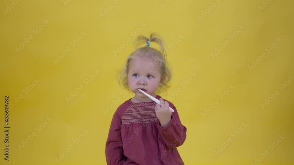 cute toddler girl in cherry colored dress funny brushing her teeth with brush on yellow studio background copy space. Dental care, beneficial habits concept, healthy lifestyle, toothpaste advertising cute toddler girl in cherry colored dress funny brushing her teeth with brush on yellow studio background copy space. Dental care, beneficial habits concept, healthy lifestyle, toothpaste advertising