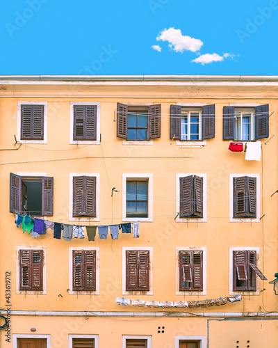 Obraz na płótnie Picturesque typical Italian slum residential house under a blue summer sky with a single cloud in Italy. Wall with many windows with shutters and linen being dried on ropes. w salonie