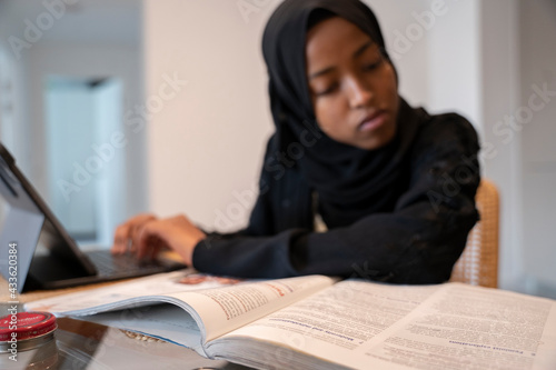 Black Muslim teenage girl doing work on a small electronic device 