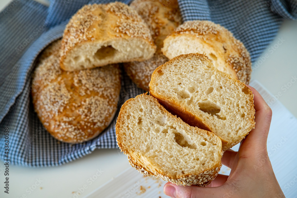 Woman holding fresh challah bread rolls hot from the oven cut into half. Crumb shot of gluten free bread buns or mini loaves with sesame seeds and golden color. Fluffy homemade bread wrapped in towel.