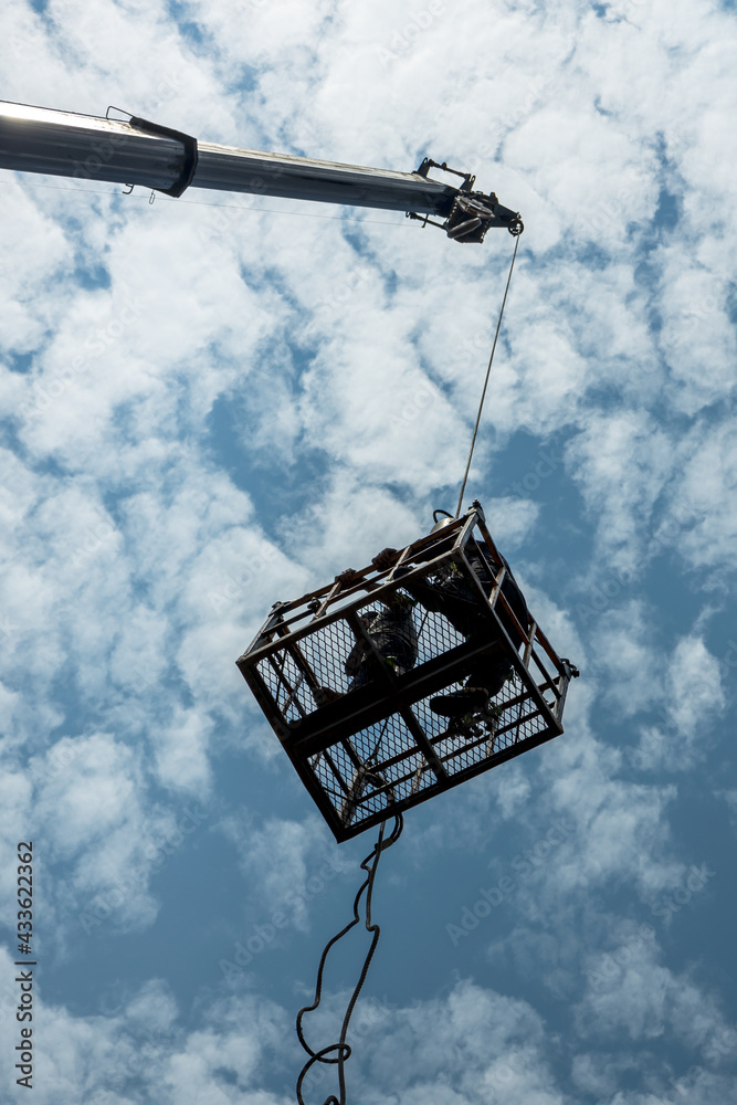 Low silhouettes of workers in steel baskets with sky clouds. Low silhouettes of workers in steel baskets with sky clouds.