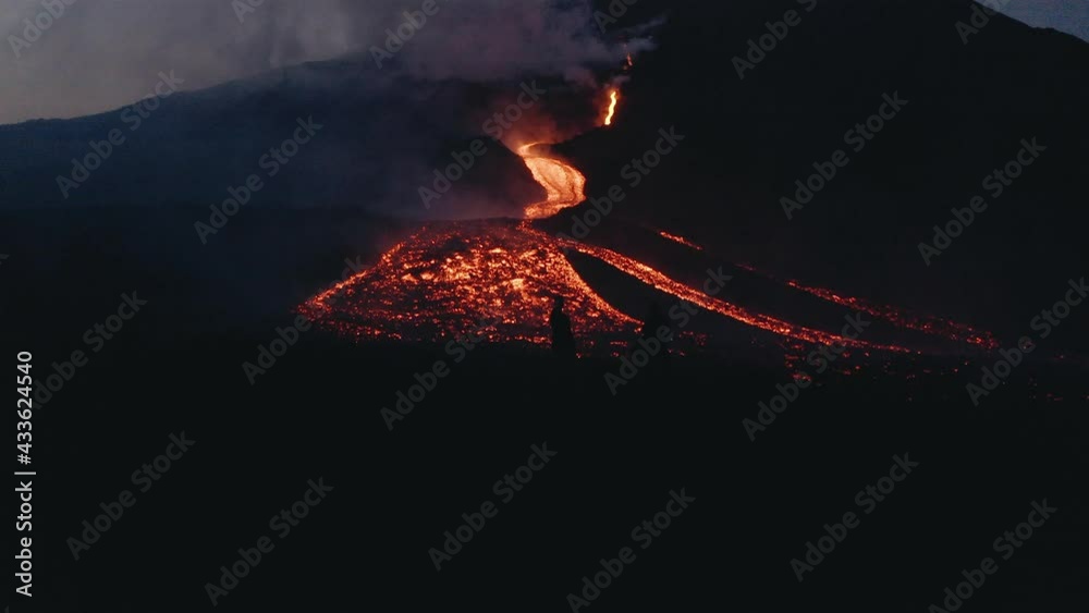 Drone aerial view of silhouette of people next to lava from Pacaya Volcano eruption at night in Guatemala