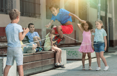 Smiling kids skipping on jumping elastic rope in european yard