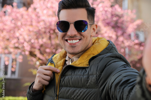 Happy man with sunglasses taking selfie outdoors on spring day