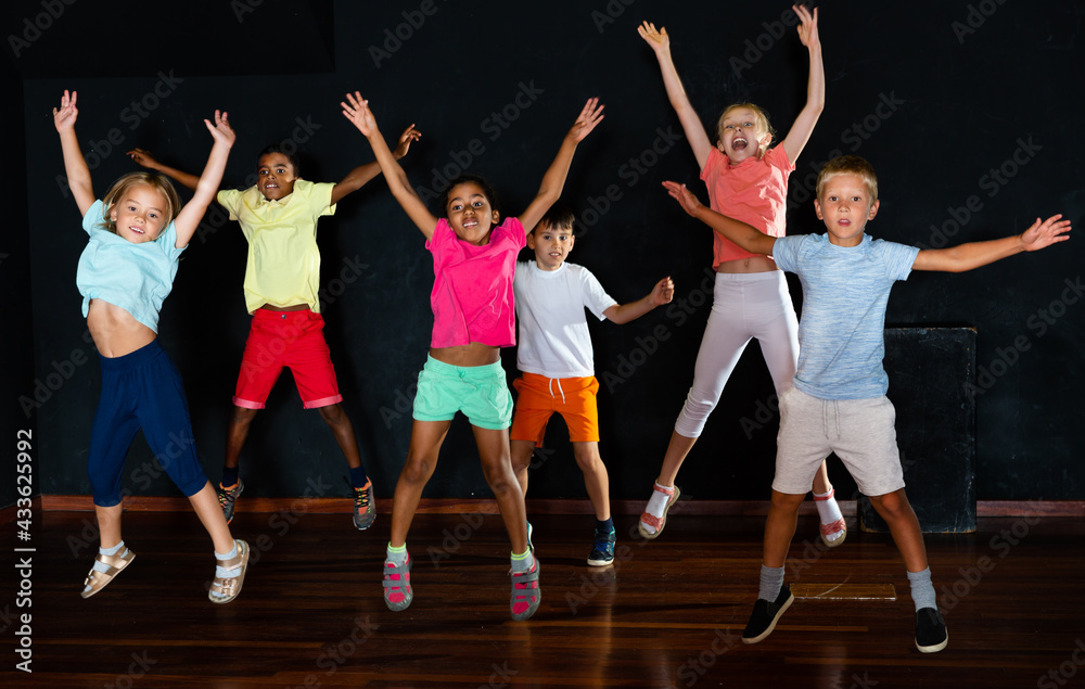 Positive children jumping while studying modern style dance in a class in the evening