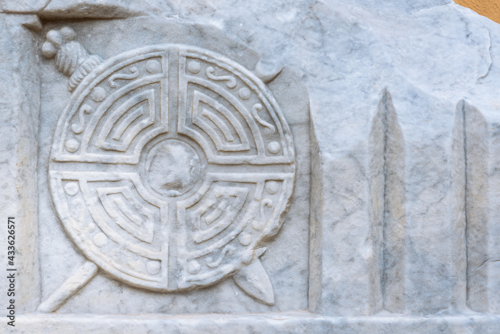 Close-up on ancient shield with swords carved on marble wall