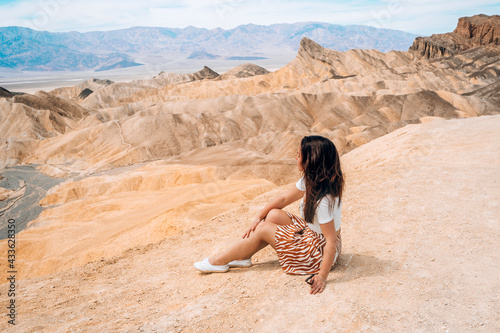A young beautiful woman in a skirt sits in the middle of the desert at Zabriskie Point against the backdrop of the mountains, Death Valley
