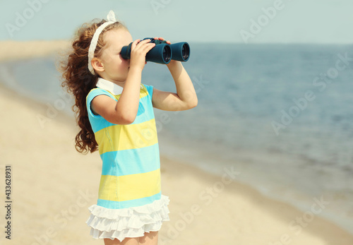 Portrait of little girl child looking through binoculars on a sea beach