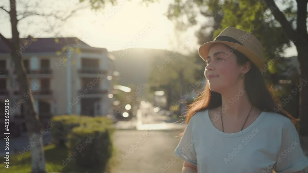 Summertime. Portrait of a young smiling woman in a straw hat, taking off her sunglasses, and looking at the camera. Sunset in the background. Pan shot. Summertime. Portrait of a young smiling woman in a straw hat, taking off her sunglasses, and looking at the camera. Sunset in the background. Pan shot.