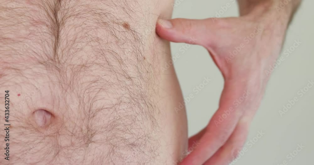Caucasian male shirtless hairy abdomen grabbing and pinching his belly fat with left hand isolated shallow depth of field unrecognizable