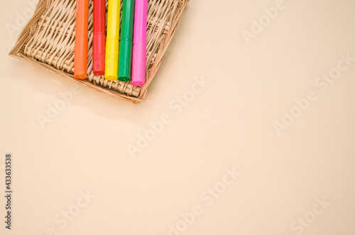 Closeup shot of colorful markers on a small woven basket isolated on a pink background photo