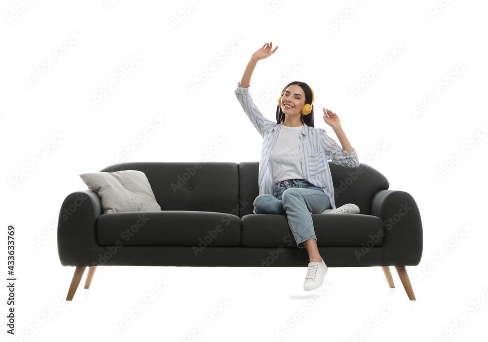 Young woman listening to music on comfortable grey sofa against white background