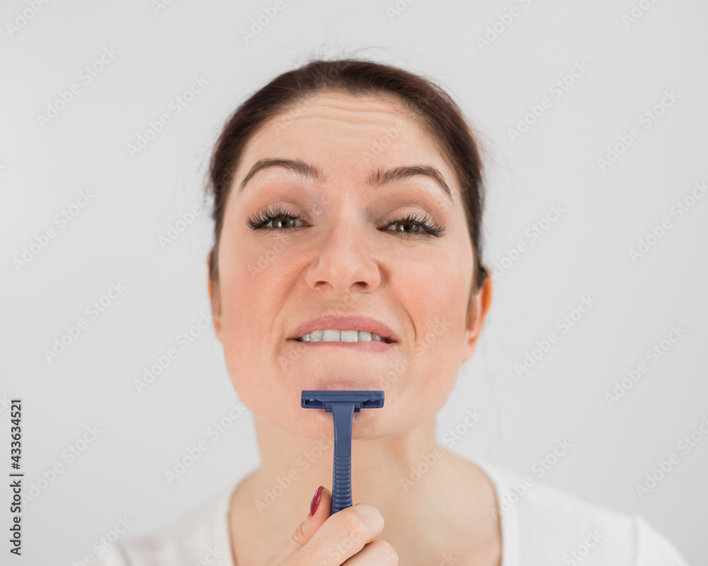 Caucasian funny woman shaves her face with a straight razor on a white background. Copy space. Caucasian funny woman shaves her face with a straight razor on a white background. Copy space.
