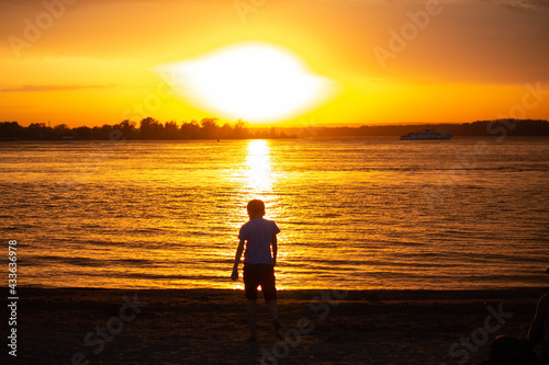 Child running at orange sunset near the water, silhouette of a man 