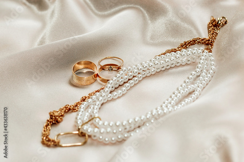 Flatley with gold jewelry and pearls on a silk background, wedding rings.
