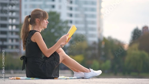 Female student sitting in summer park reading textbook outdoors. Education and sudy concept. photo