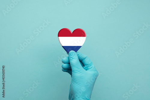 Hands wearing protective surgical gloves holding Netherlands flag heart
