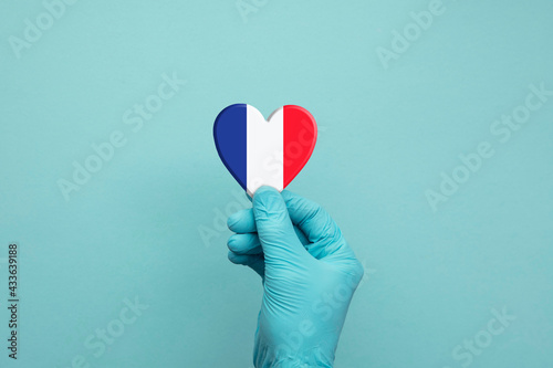 Hands wearing protective surgical gloves holding France flag heart