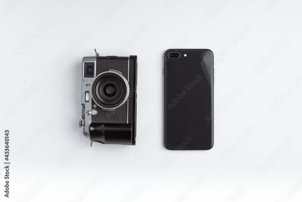 A mirrorless camera and smartphone lays aside on a white background