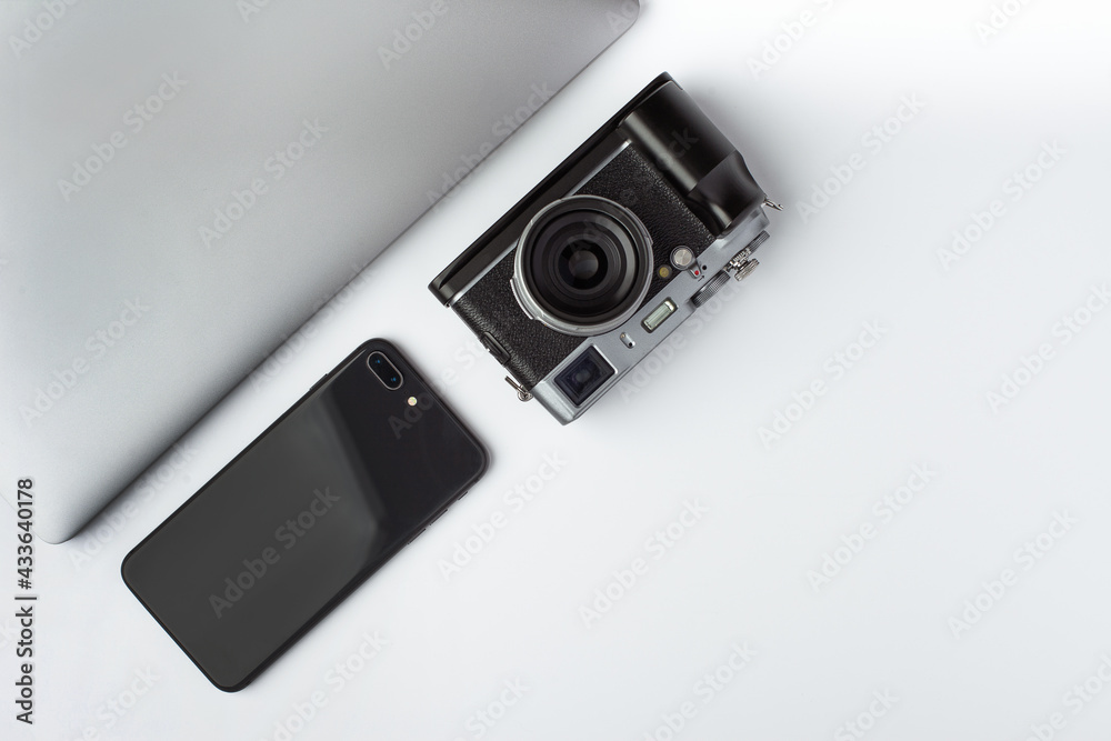 A mirrorless camera, laptop and smartphone lays aside on a white background A mirrorless camera, laptop and smartphone lays aside on a white background