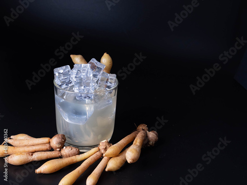 Cold finger root juice in clear glass and fresh finger root on a black wood floor, an alternative to COVID-19
