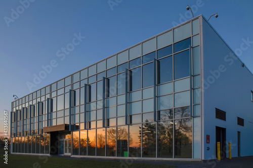 Low-rise commercial or institutional building glass and aluminum facade at dusk with sunset reflecting on windows, security cameras, nobody
