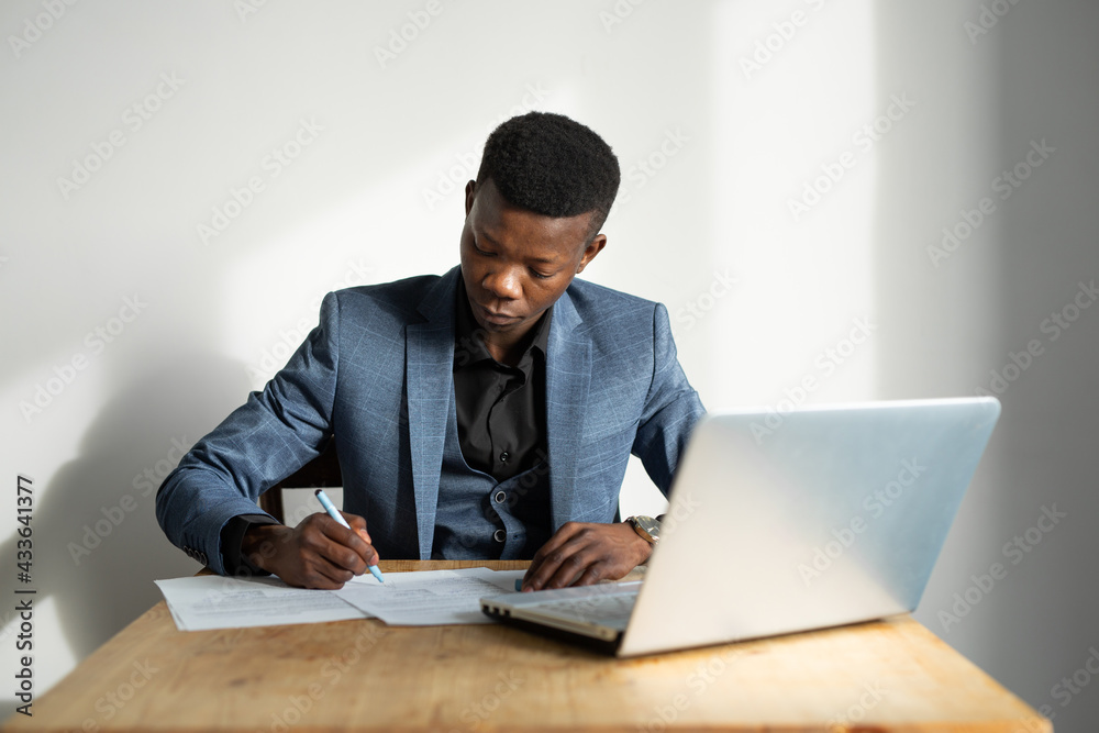 handsome young african man in suit in office at table with laptop handsome young african man in suit in office at table with laptop