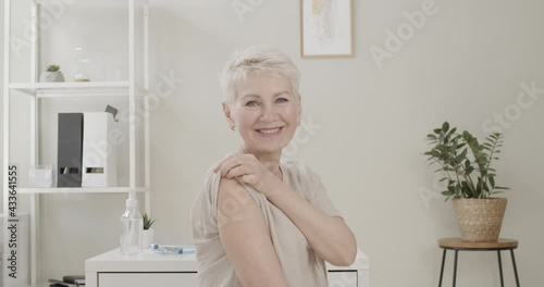 Happy smiling senior woman sitting at hospital after receiving vaccine dose, showing arm with band-aid. Vaccination or jab concept