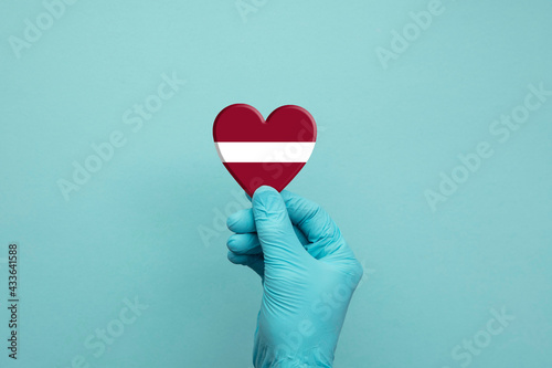 Hands wearing protective surgical gloves holding Latvia flag heart