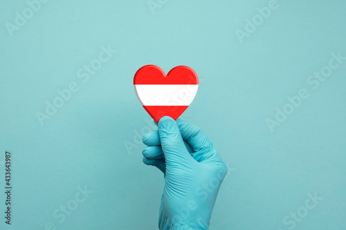 Hands wearing protective surgical gloves holding Austria flag heart