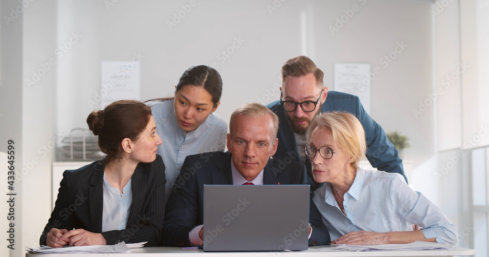 Multiethnic business team looking at laptop screen while working together in office Multiethnic business team looking at laptop screen while working together in office