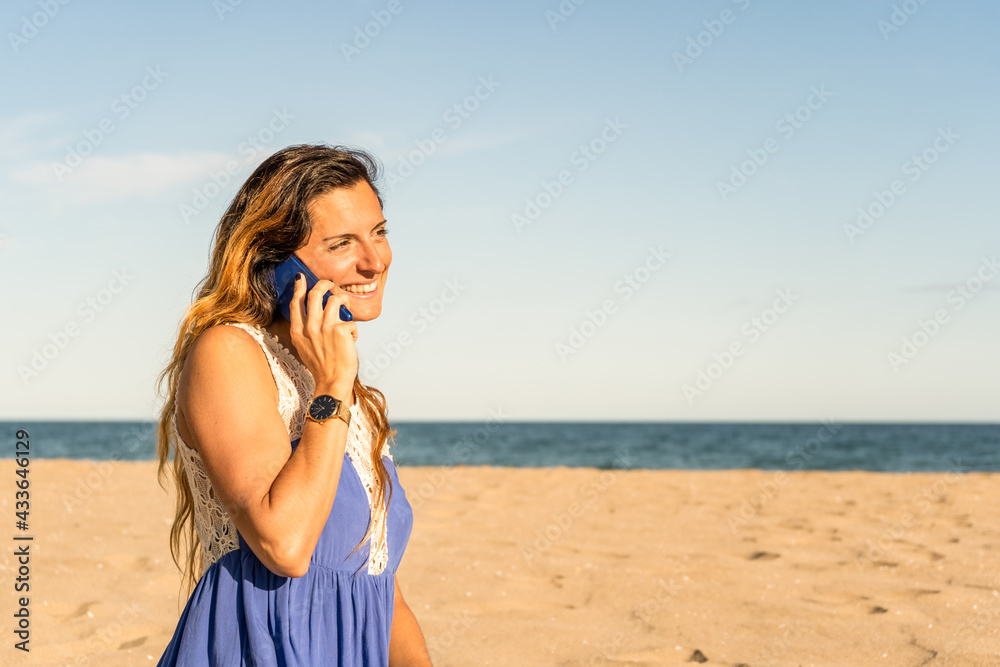 Happy stylish female talking on cell phone on beach at sunset.Woman using smartphone, making a call in summer holidays destination. Happy stylish female talking on cell phone on beach at sunset.Woman using smartphone, making a call in summer holidays destination.