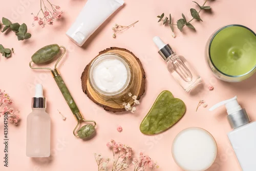 Obraz Cosmetic products - Jade roller and gua sha massager with cream and serum bottles at pastel background. Spa background. Top view with copy space.