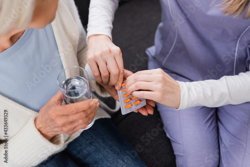 partial view of nurse giving medication to aged woman holding glass of water