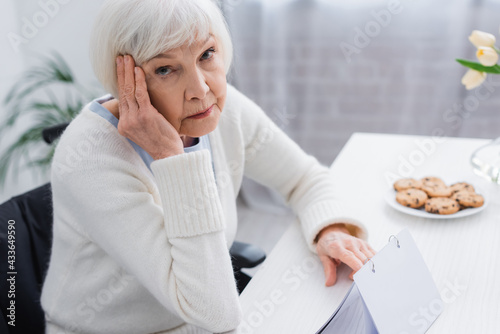 aged woman, sick on dementia, touching head while looking at camera near calendar